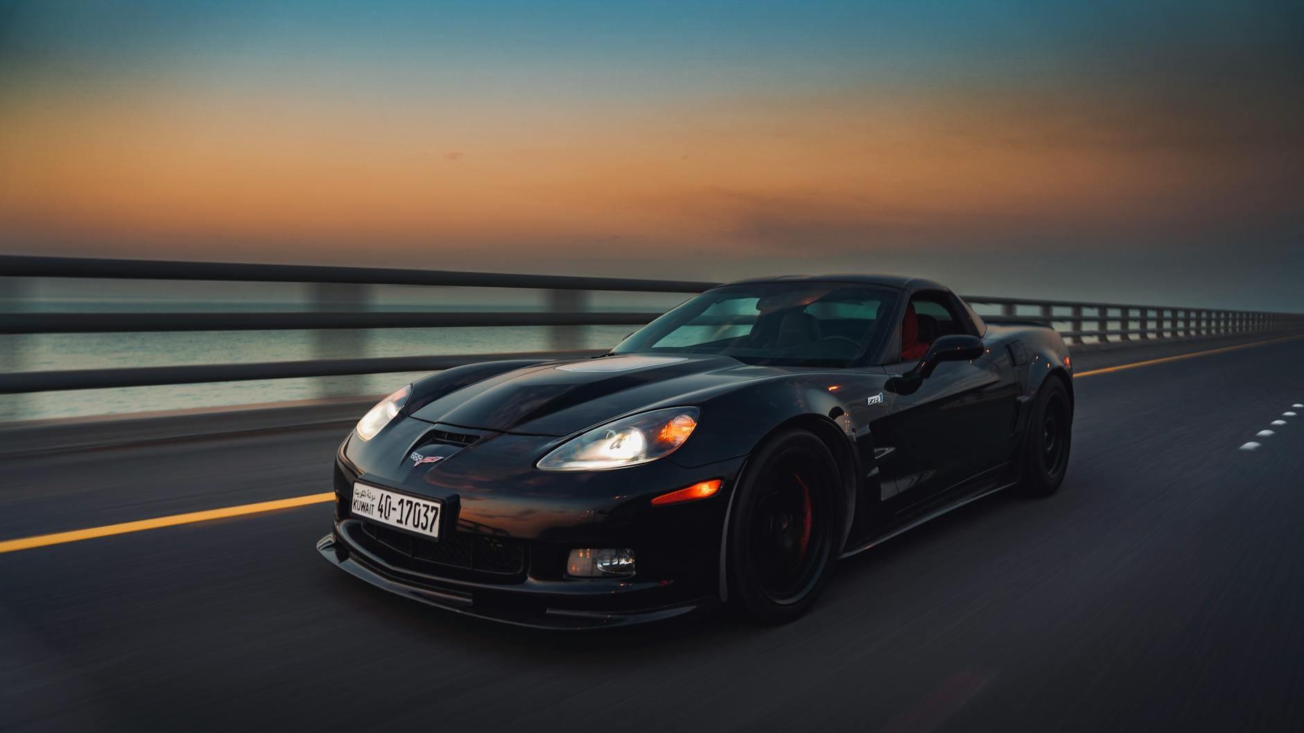 Czarny sportowy samochód jadący szybko po moście nad morzem o zmierzchu