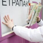 Osoba w białej kurtce wrzuca kartony do fioletowego pojemnika na recykling