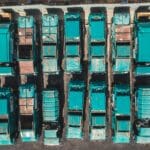 Turkusowe śmieciarki sfotografowane z góry, ustawione w równych rzędach