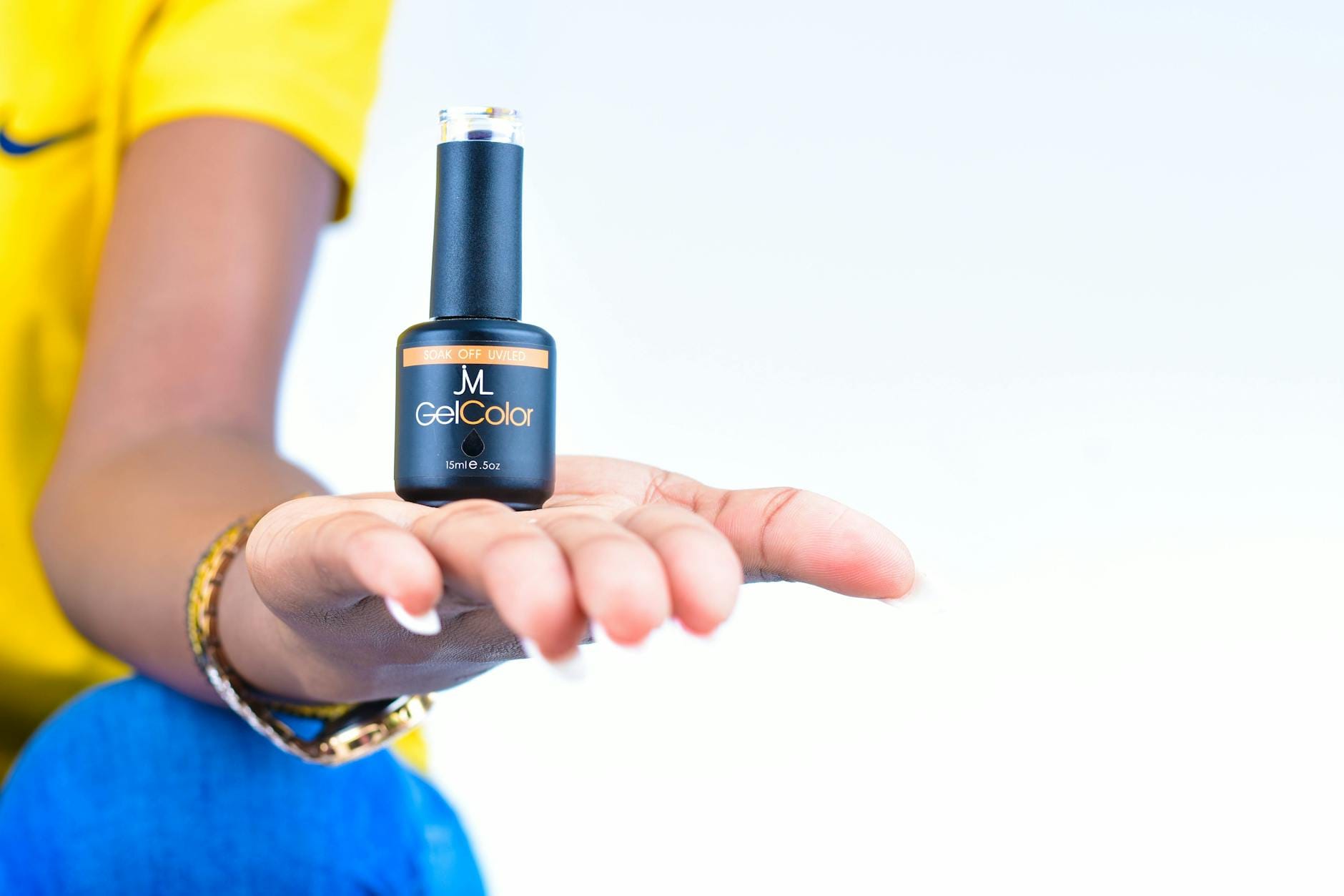 Dłoń kobiety prezentująca buteleczkę lakieru hybrydowego na jasnym tle